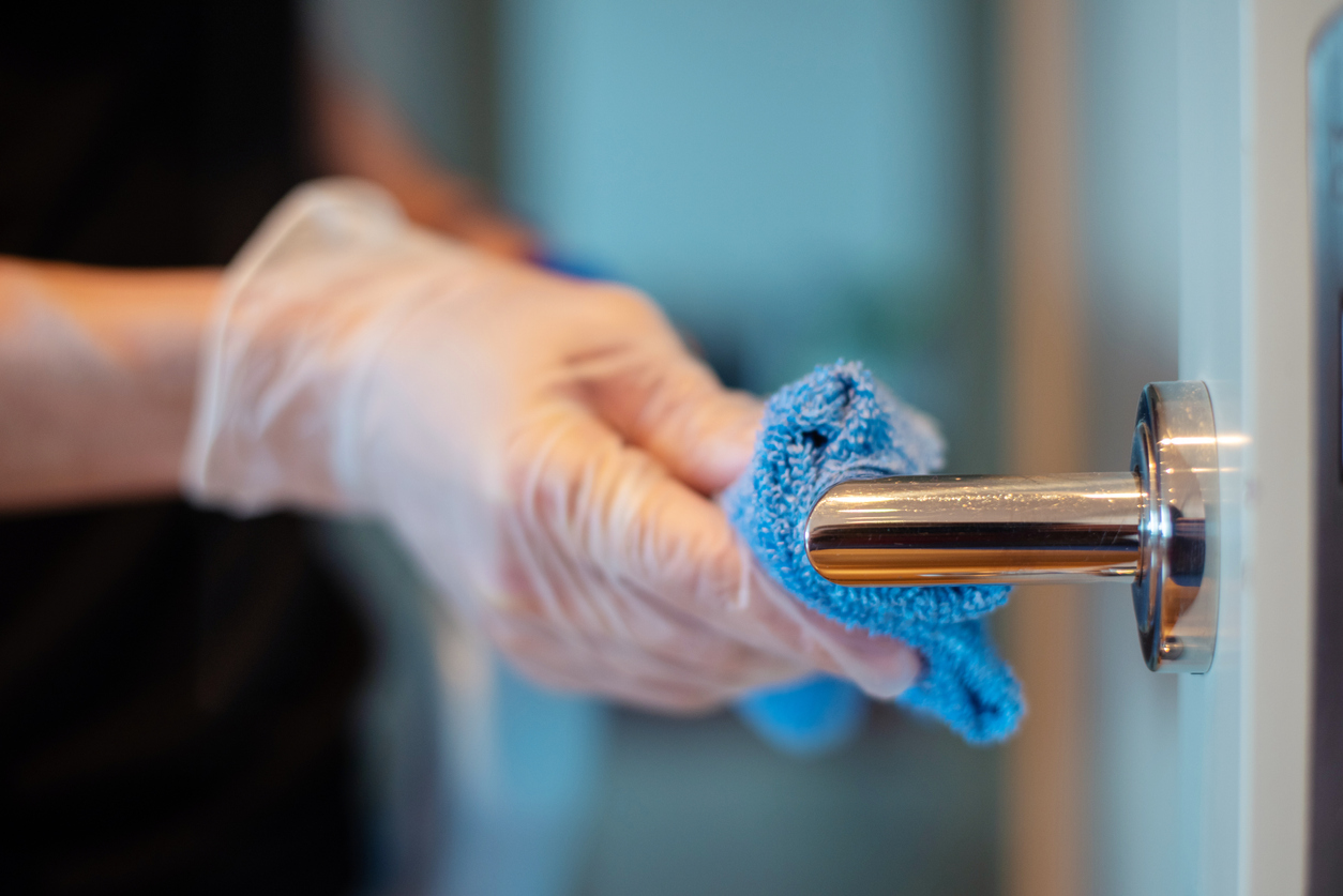 Closeup of the hands of a person disinfecting a door knob