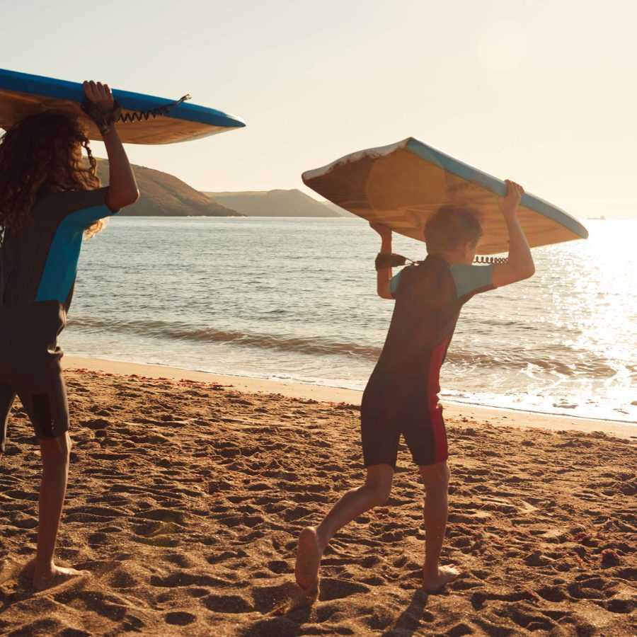 Two kids on beach with bodyboards on holiday in UK